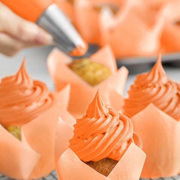 A person using Chefmaster Neon Brite Orange food coloring to decorate cupcakes with orange frosting.