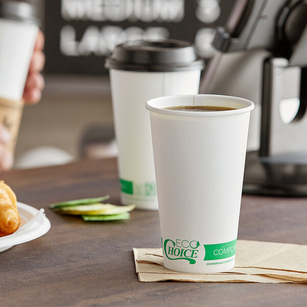 A close-up of a white EcoChoice paper hot cup filled with coffee on a table with coffee cups and croissants.