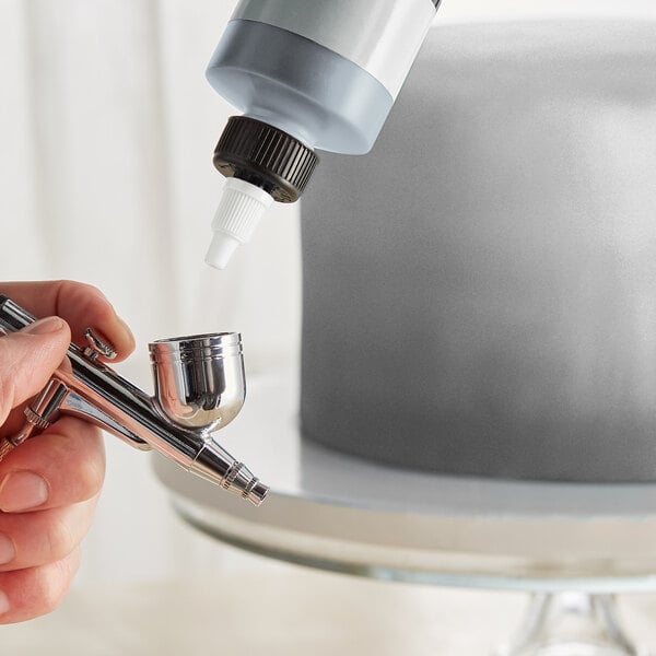 A finger uses Chefmaster Metallic Silver Airbrush Color to paint a cake.
