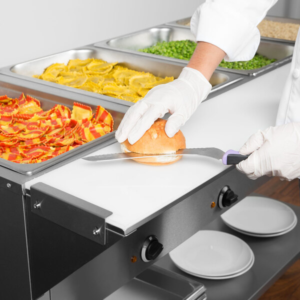 A person in white gloves cutting food on an Avantco cutting board in a kitchen.