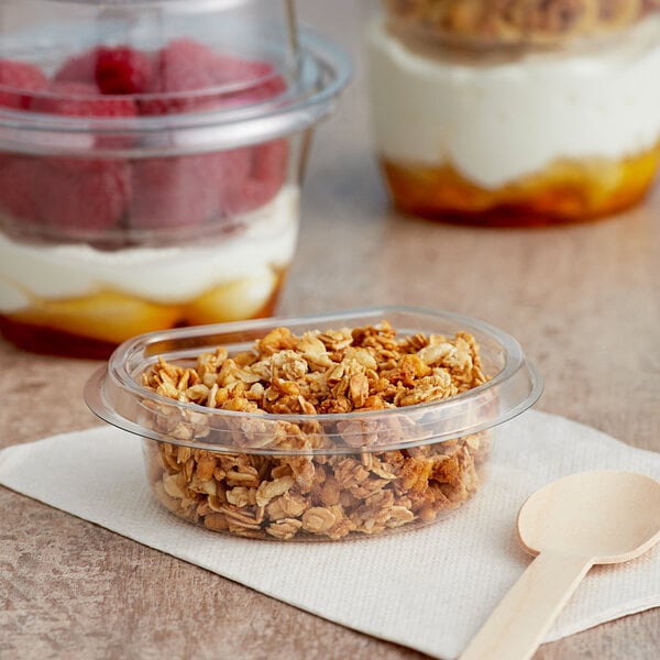 A bowl of granola and yogurt with a spoon in a Clear PET Parfait Cup.