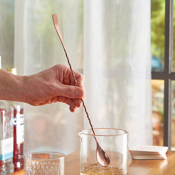 A hand using an Acopa copper Japanese bar spoon in a glass of liquid.