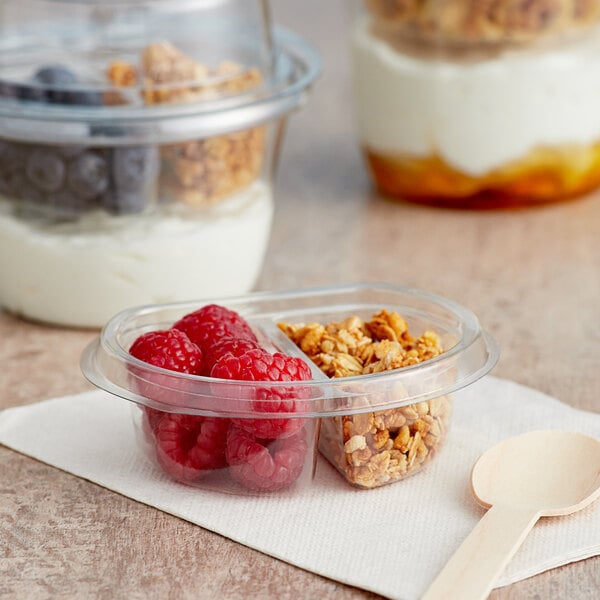 A Clear PET parfait cup with a double compartment and a wooden spoonful of cereal and raspberries.