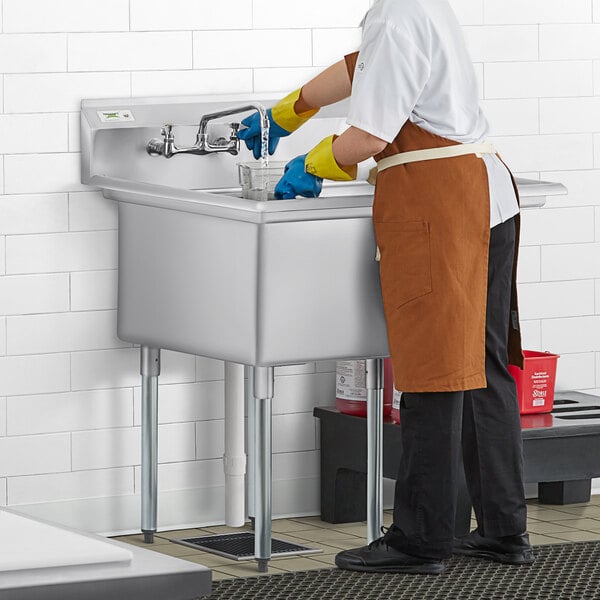 A man in a uniform washing a Regency commercial sink with a right drainboard.
