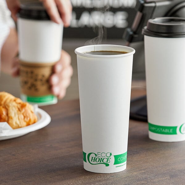 A person holding a white EcoChoice compostable paper hot cup filled with coffee and a croissant.