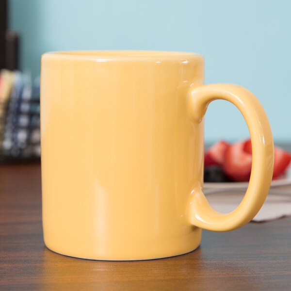 A close up of a yellow Tuxton mug on a table full of yellow liquid.