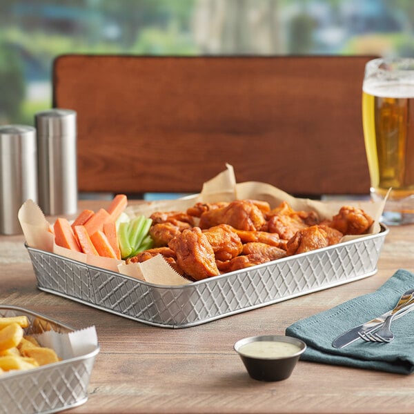 A Tablecraft lattice stainless steel rectangular platter with chicken wings and fries on a table.