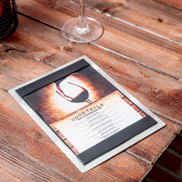 A Menu Solutions Alumitique aluminum menu board on a table with a wine glass and a menu.