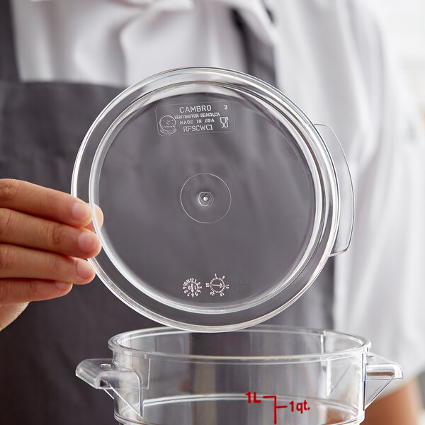 A hand holding a clear lid over a clear food storage container.