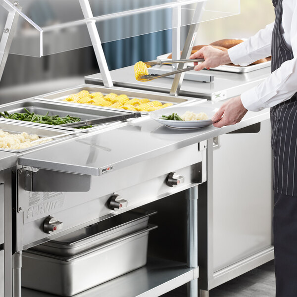 A chef using a ServIt solid drop down side tray on a steam table to hold a plate of food.