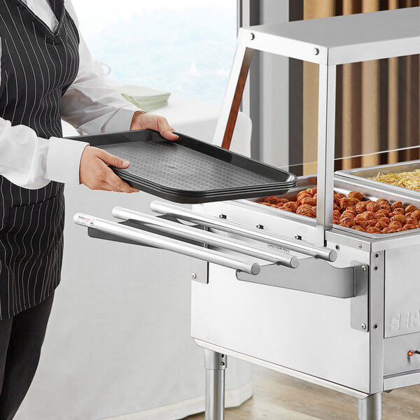 A woman using a ServIt tubular tray slide to hold a tray of food on a table at a hotel buffet.
