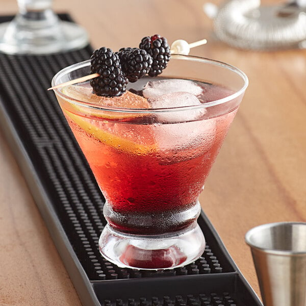 An Acopa stemless martini glass filled with a cocktail with blackberries and a lemon wedge on a bar.