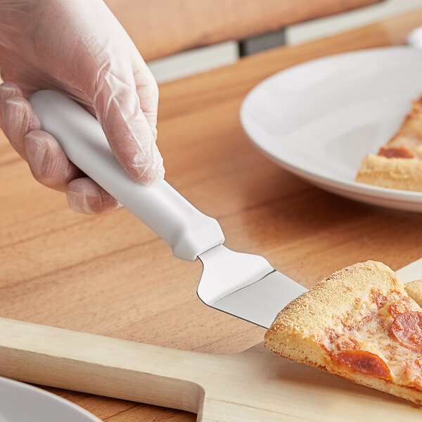 A person's hand using a Choice white pie server to cut a slice of pizza.