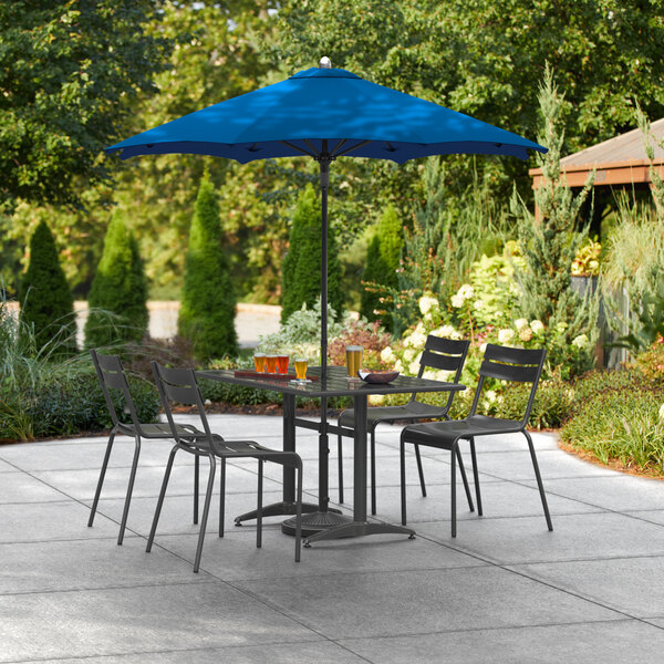 A Lancaster Table & Seating cobalt umbrella on a table with chairs on a patio.