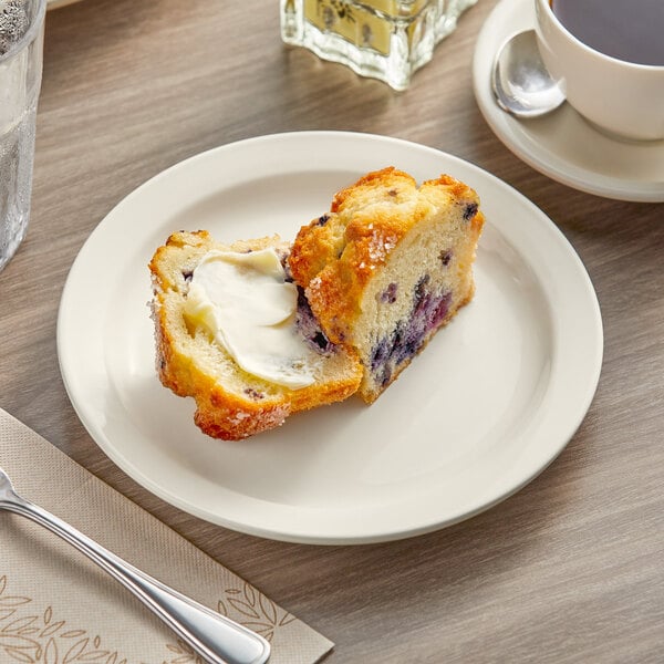 An Acopa narrow rim stoneware plate with a blueberry muffin and a cup of coffee on a table.