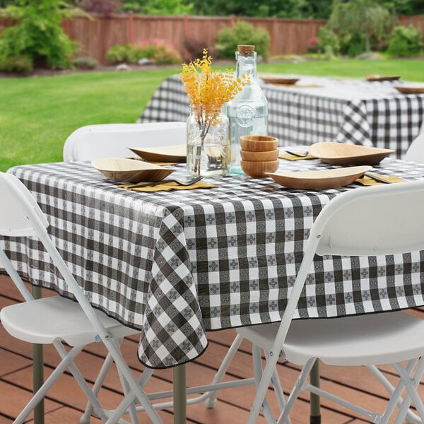 A table set with a black and white checkered vinyl tablecloth on a table outdoors.