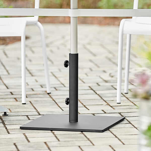 A black Lancaster Table & Seating umbrella base on a table outdoors with white chairs.