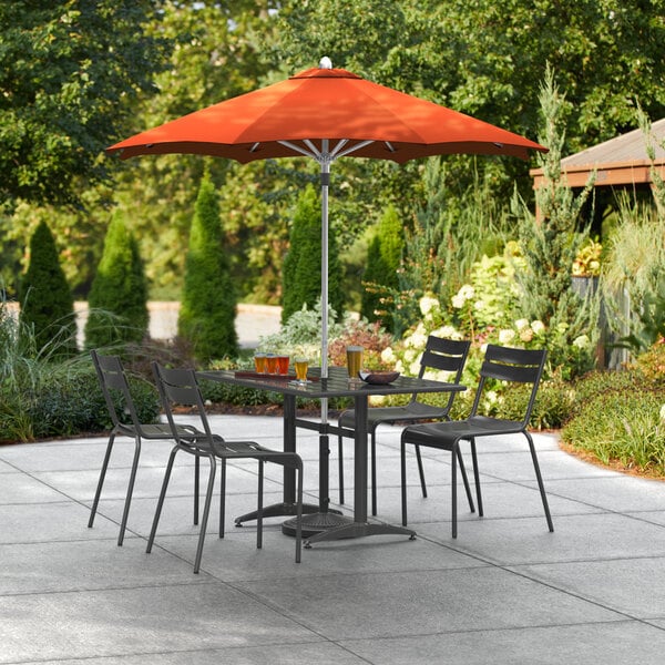 A table and chairs under a Lancaster Table & Seating Papaya umbrella on a patio.