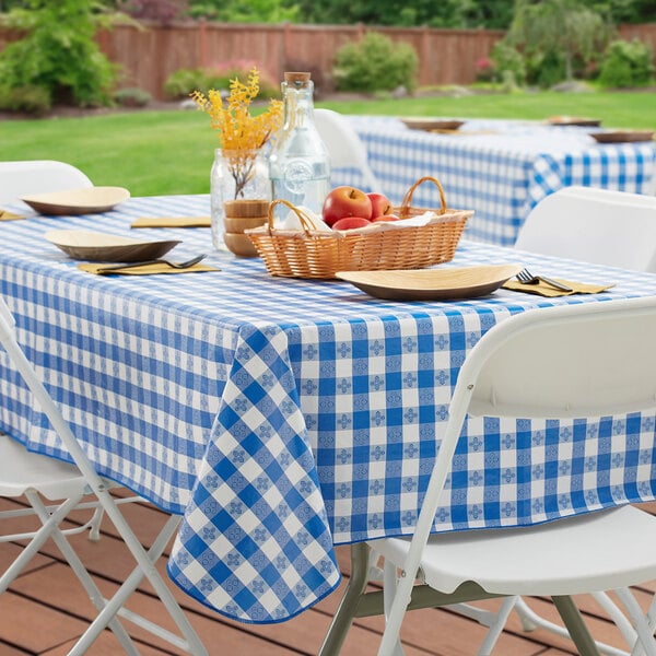 A picnic table with a Choice royal blue and white checkered vinyl tablecloth and a basket of fruit.