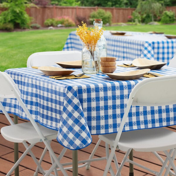 A wooden table with a Choice blue and white checkered vinyl table cover set for a picnic.