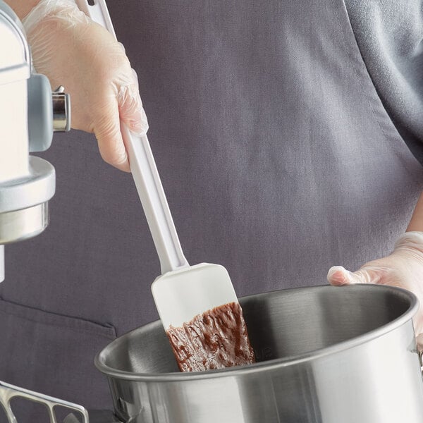 A person using a white Choice spoonula to mix brown liquid in a metal pot.