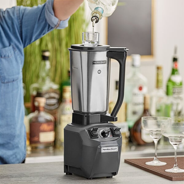 A person using a Hamilton Beach culinary blender to make a drink in a wine glass.