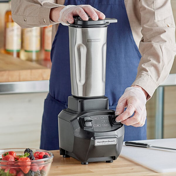 A man using a Hamilton Beach commercial drink blender on a counter to blend fruit.