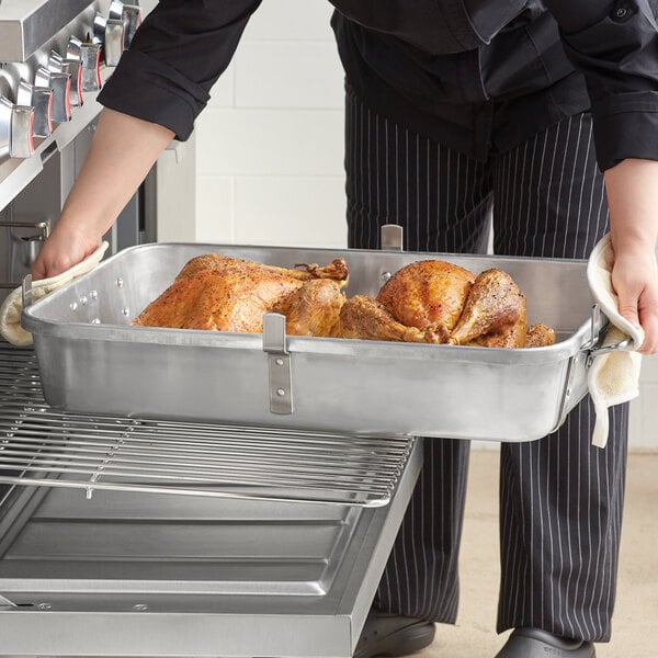 A woman in a chef's uniform using a Choice aluminum roaster pan to hold a tray of cooked turkey.