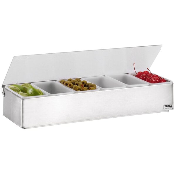 A Vollrath stainless steel condiment bar on a counter with fruit.
