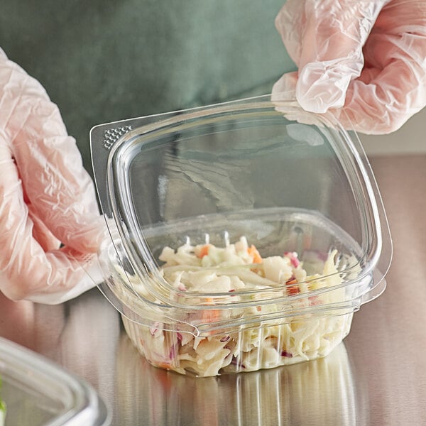 A person in gloves holding a Choice clear plastic deli container of food.