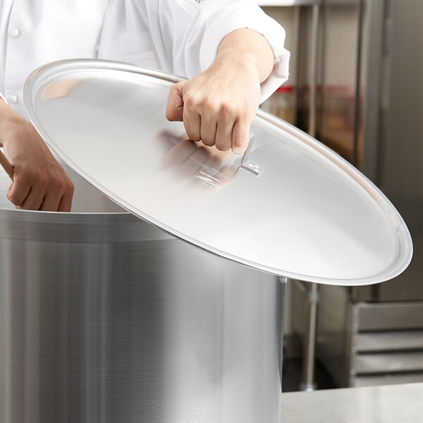 A hand holding a Vollrath Wear-Ever domed aluminum pot / pan cover over a large pot.