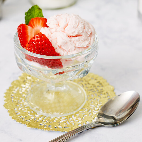A Libbey sherbet glass filled with a bowl of ice cream topped with strawberries and mint leaves on a gold place mat.
