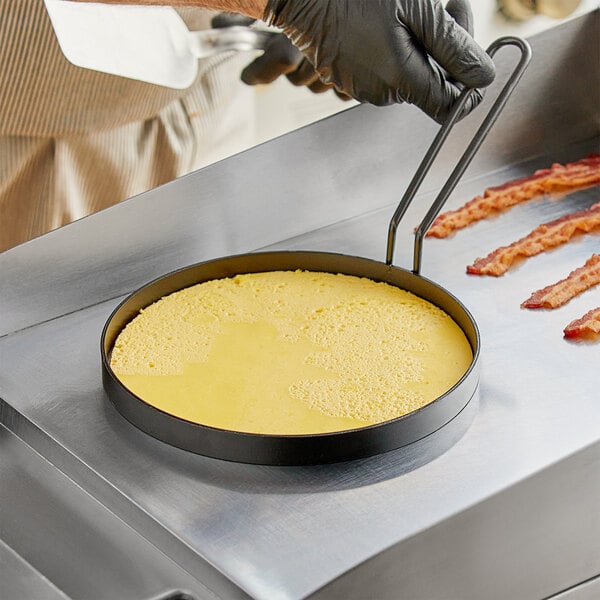 A person cooking bacon in a Vigor non-stick egg ring on a pan.