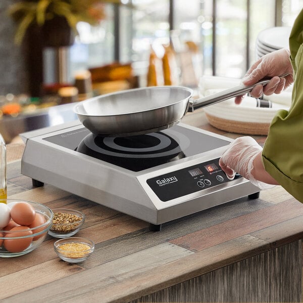A person cooking on a Galaxy stainless steel countertop induction range.