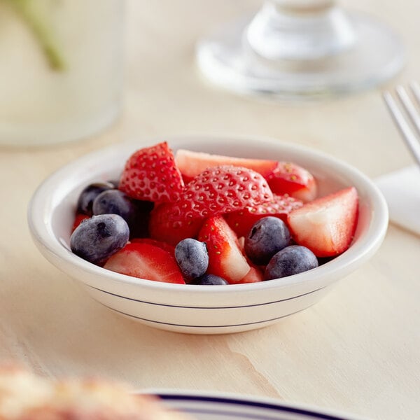 A bowl of fruit with strawberries in an Acopa ivory stoneware bowl with blue bands on a table.