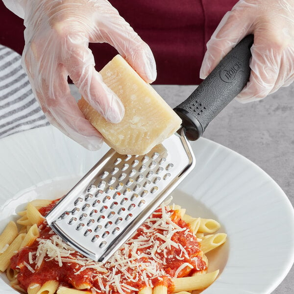 A person grating cheese over pasta using a Choice stainless steel grater with a black handle.