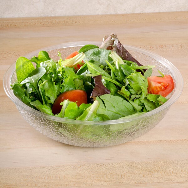 A bowl of salad with tomatoes served in a clear Cambro pebbled bowl.