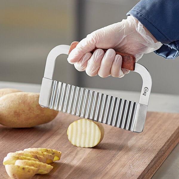 A person wearing a glove using a Choice 7" Crinkle Knife to cut a potato.