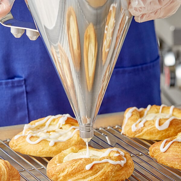 A person using a Choice stainless steel confectionery dispenser funnel to pour cream into a pastry bag.