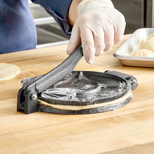 A person using a Choice metal tortilla press to flatten dough.