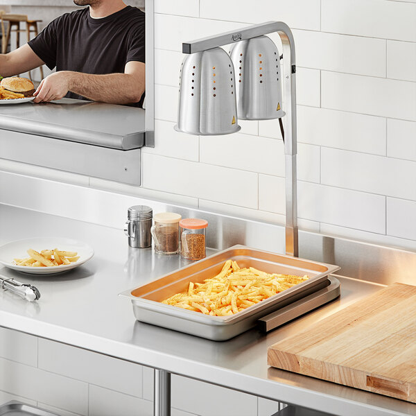 A man using an Avantco countertop heat lamp to cook french fries.