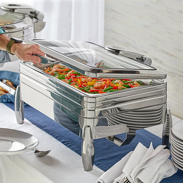 A person using an Acopa Manchester dual purpose chafer to serve food on a table outdoors.