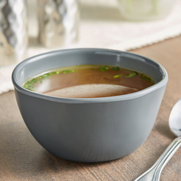 An American Metalcraft Crave storm melamine bouillon cup filled with broth on a table with a spoon.