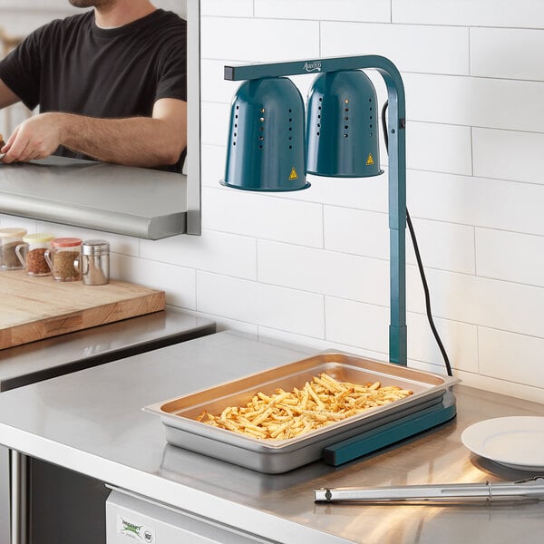 A man using an Avantco green free standing countertop heat lamp to cook food.