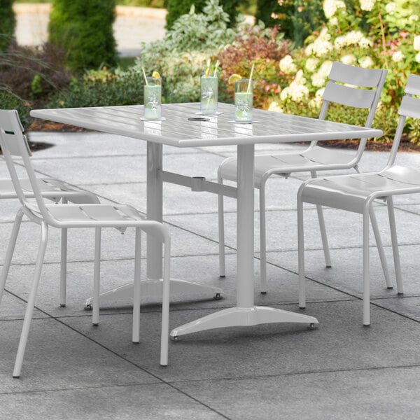 A white Lancaster Table & Seating outdoor dining table with a white umbrella and chairs on an outdoor patio.