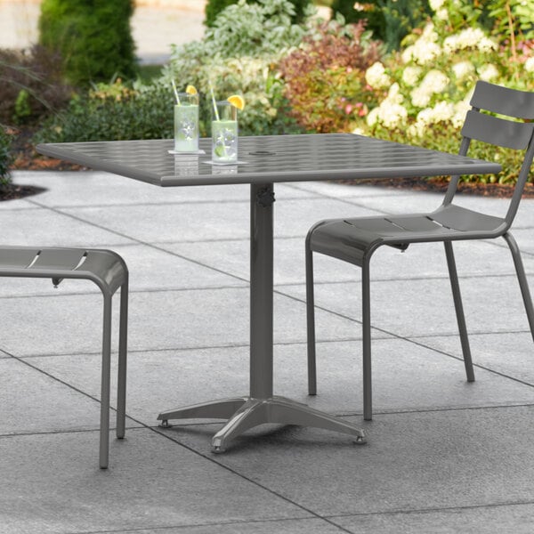 A gray Lancaster Table & Seating outdoor table with a chair and umbrella on a patio.