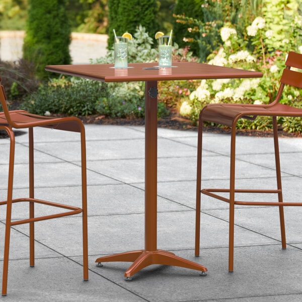 A brown Lancaster Table & Seating bar height outdoor table with two chairs on a patio.