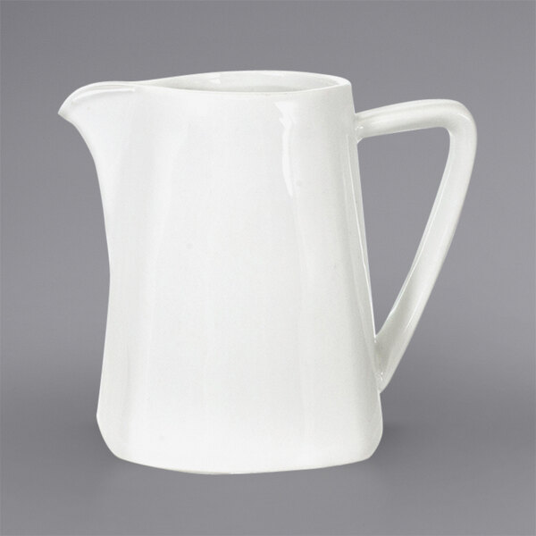 A white International Tableware Elite porcelain creamer with a handle.
