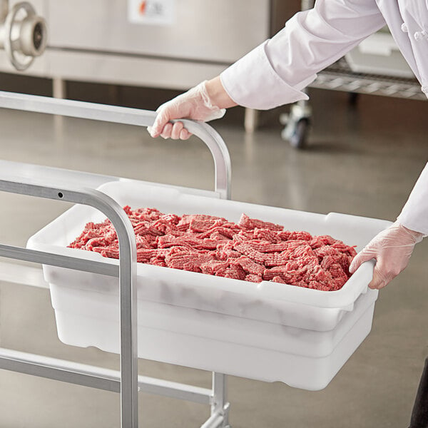 A person in white gloves holding a Choice white meat tote filled with raw meat.