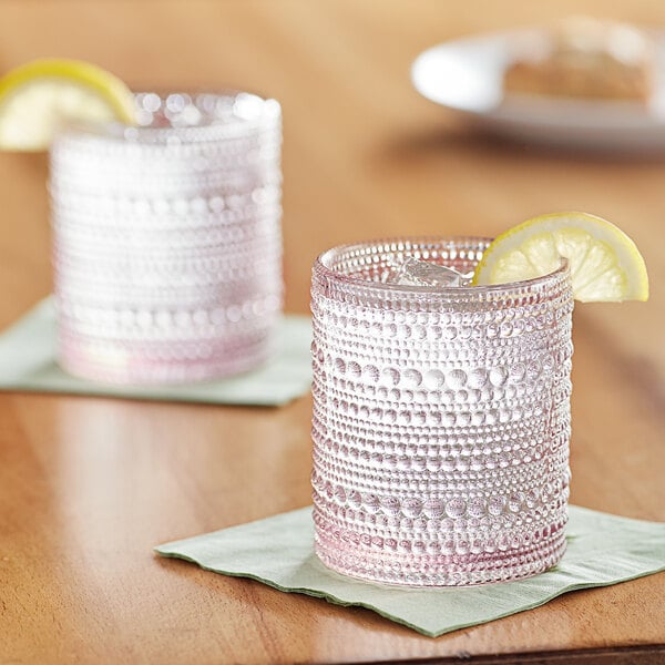 Two Fortessa Jupiter pink double old fashioned glasses with ice and lemon slices on a table.